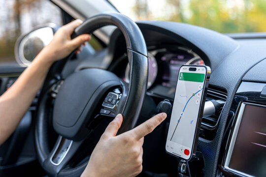 A woman in a car holds a mobile phone with a GPS navigation map.