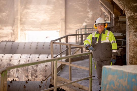 A worker in a helmet and equipment stands against the backdrop of a cement plant workshop. Work technology, cement production. People working in heavy industry.