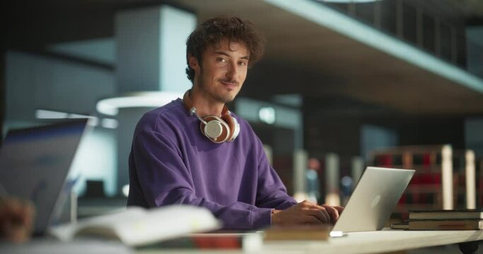 Portrait of a Handsome European Student Studying in a Traditional Library. Young Male Looking at Camera and Smiling. Scholar Working on Laptop Computer in College, Researching Academic Topics Online
