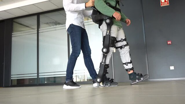 Mechanical exoskeleton, physiotherapist walking with unrecognizable disabled person with robotic skeleton, physiotherapy in a modern hospital: