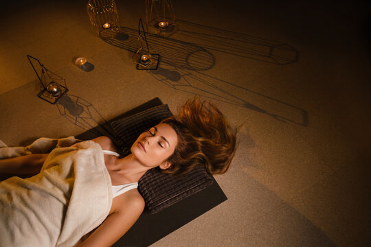 A woman lies on the floor covered with a blanket with her eyes closed and relaxes after a workout , shavasana pose
