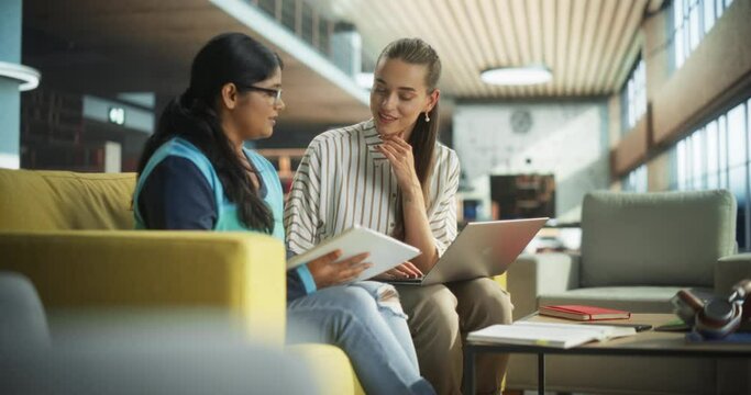 Two Diverse Friends and Classmates Working on a Collaborative Team Project in an Academic Library. Young Indian and Caucasian Women Using Laptop Computer for Online Learning and Virtual Lectures