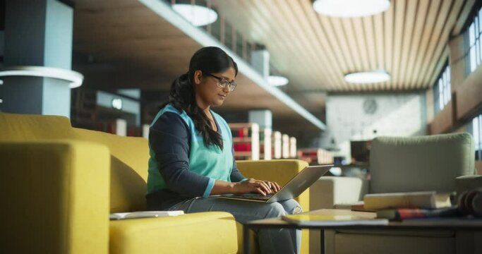 Smart Indian Female Student in Glasses Working on Software Development Assignment in a Quiet Public Library. Young South Asian Woman Using Laptop Computer and Preparing for Examination in College