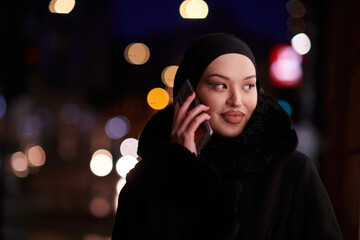 uropean Muslim Hijabi Business Lady checking her phone on urban city street at night