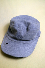 The gray cloth hat is in a worn condition with several tears. Cream background