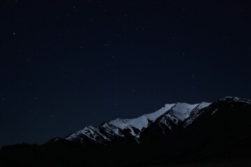 Night sky with countless stars twinkling brightly above snow-capped mountain peaks