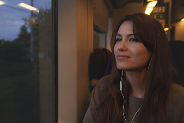 A girl on the train listens to music. The girl listens to music through wired headphones.
