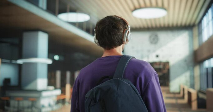 Young Man Walking Inside a Library Building with a Backpack. Stylish Male Student Walking in College, Office Building, Shopping Center with a Book Store. Footage From the Back