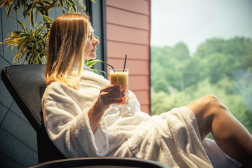 Woman in white bathrobe lying on sofa and relaxing with orange cocktail at SPA. - obrazy, fototapety, plakaty