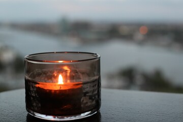 a lit candle on a table by the ocean on a windy day