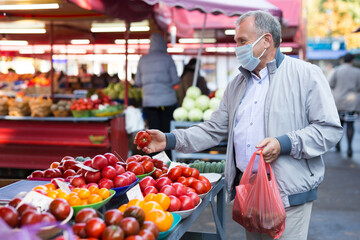 Man in face mask choosing tomatoes in greengrocery
