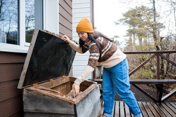 Young girl taking firewood out from the woodshed box outside the cabin in winter.