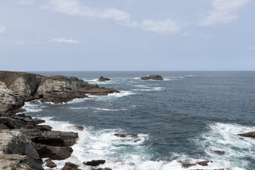 high-angle photo of a jagged, rocky coastline with small islands in the background under a cloudy sky, ai generative