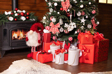 Black cast iron fire place with wood burning inside of it near Christmas tree. Fragment decor of...
