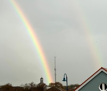 Double rainbow in grey sky near church, de Koog Texel