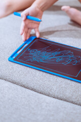 Child drawing with a blue pen on an electronic black board surface tablet