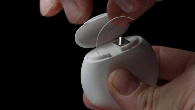 A White Dental Floss Container, a man pulls out a length of floss and cuts it using the designated area on the packaging.