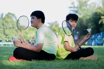 Asian boy holding white shuttlecock and badminton racket to play outdoor badminton with friend in...