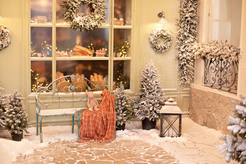Xmas festive street with snow, bench and baking in showcase near a cafe bakery. Christmas decor: gift, toys, trees, garland fir branches, glowing light bulbs. Cozy outdoor cafe on Christmas eve.	
