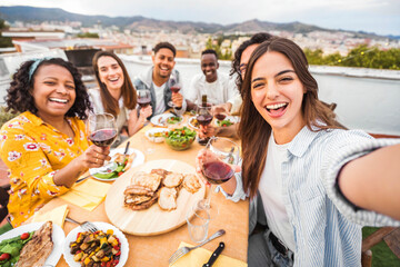 Happy friends having fun at rooftop dinner party - Group of young people taking selfie photo at outdoors dining table - Life style concept with guys and girls eating food and drinking wine together