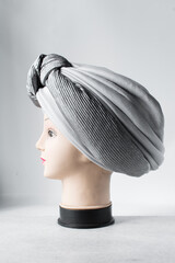 Grey turban on a mannequin head, pleated Grey fashion turban on a white background