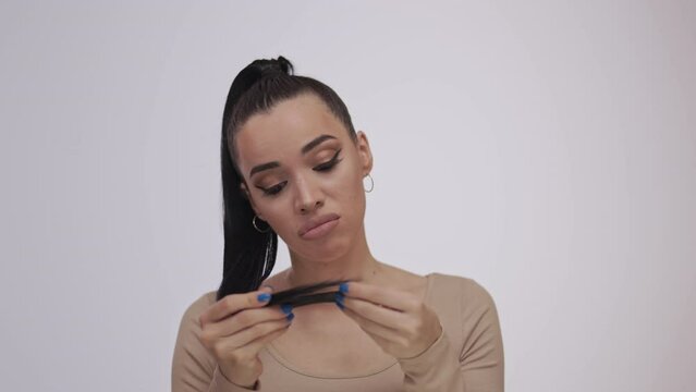 A beautiful brunette examines the ends of her hair. Damaged hair and unhappy face