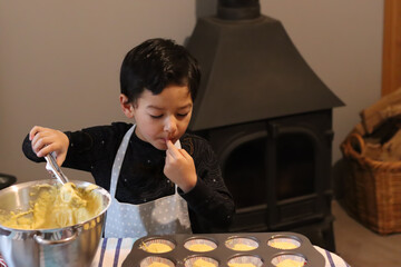 Baking concept Child taste a cake lick his finger play messy fancy cup cake muffin. Boy hand...