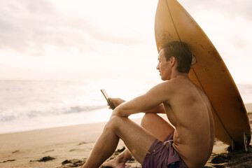 Handsome surfer with his surfboard. Young man listening the music while enjoy at the beach.