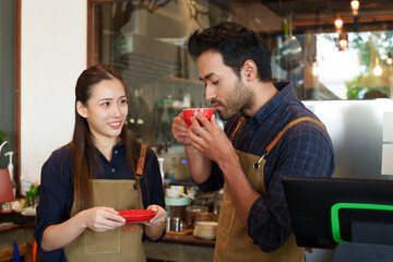 A young Indian businessman is drinking red cup of coffee that his Asian girlfriend made for her boyfriend. The girl stared at cute smile. In their coffee shop, the cafe is small family business.