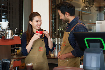 Asian businesswoman couple holding red coffee mugs smiling at indian.  of them met each other's eyes with  happy smile as they prepared to welcome customers  would come to use service at cafe.