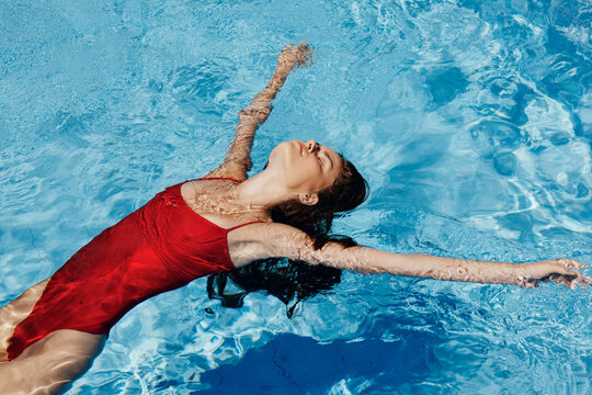 Happy woman swimming in pool in red swimsuit with loose long hair, skin protection with sunscreen, concept of relaxing on vacation.