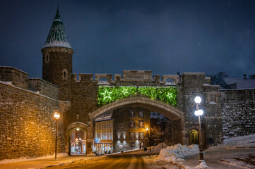 St-Jean Street through the Saint-Jean Gate with Christmas winter holidays decorations on a snowy night, entry points through the fortified walls surrounding Old Quebec City, Canada (December 2022).