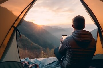 Male traveler camping on the mountain while playing on his phone