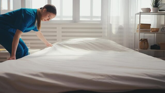 Young nurse making bed in a hospital ward, preparing room for patient, service