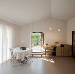 Front view of the kitchen area with a table and chairs on the left, furniture on the right. The interior is modern and minimalist.