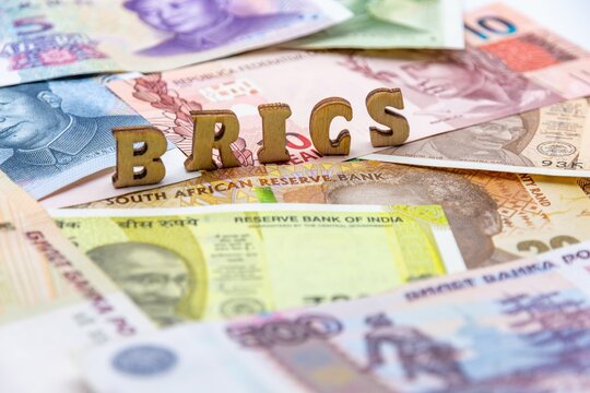 Closeup of a stack of various currency banknotes with the letters BRICS on top