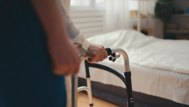 Nurse assisting senior female patient with using walking frame at hospital ward