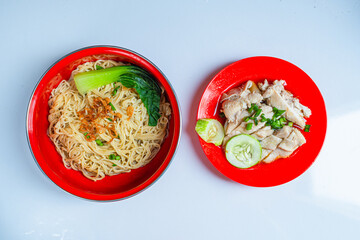 Mie Hainan or Hainan noodles with steamed chicken on a red plate and bowl. Malaysian or Singapore traditional food. Isolated white background.