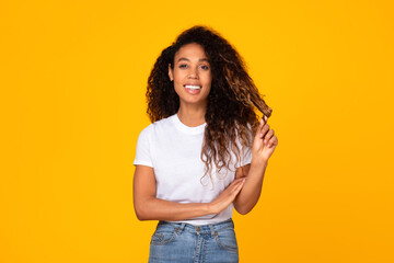 Cheerful black woman with curly hair posing against yellow backdrop