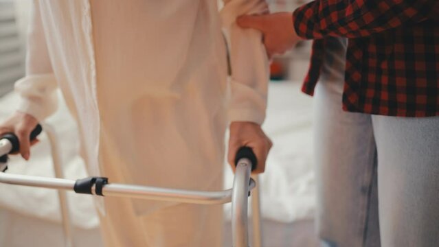 Caring volunteer helping senior woman to stand up with walking frame in hospital