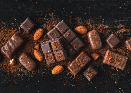 Various chocolate candies sprinkled with coffee closeup on a black wooden table in the dark