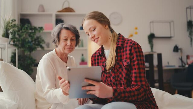 Happy woman showing family photos on tablet to loving granny in a nursing home