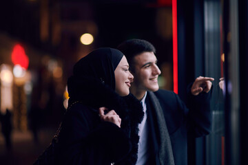 Happy multicultural business couple walking together outdoors in an urban city street at night near...
