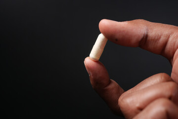 Close up of man hand holding capsule against orange background 