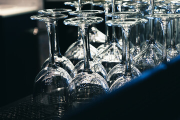 Beautiful new wine glasses stand in even rows in a bar in blue colors. Empty glass clean upside-down stemware in nightclub or a restaurant. Party time. Soft focus and blurred cold background