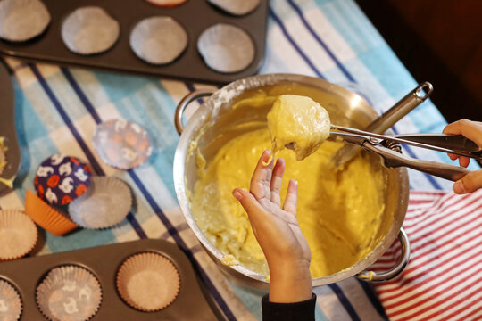 Baking concept Child play messy fancy cup cake muffin. Boy hand holding scoop putting cake batter in a muffin tray.