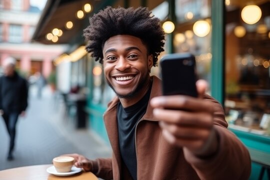 happy african american man takes a selfie on a smartphone against the background of a cafe