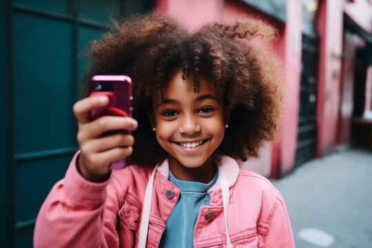 happy african american child girl takes a selfie on a smartphone against the background of a house