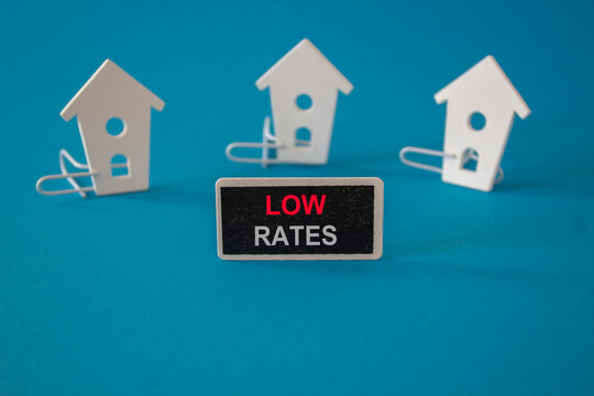 Low house rates symbol. Wooden houses sits next to a wooden black board with the word Low rates. Beautiful blue background. Business and low house rates concept.