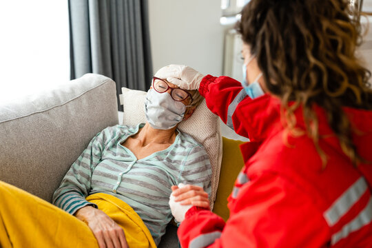 Emergency medical technician in uniform visiting senior female patient with eyeglasses and face mask for medical check up during Covid-19.